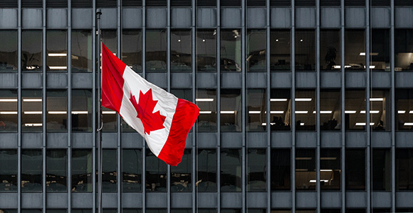A waving Canadian flag in front of a large city skyscraper. 