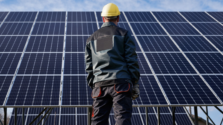 Un homme debout devant des rangées de panneaux solaires. 