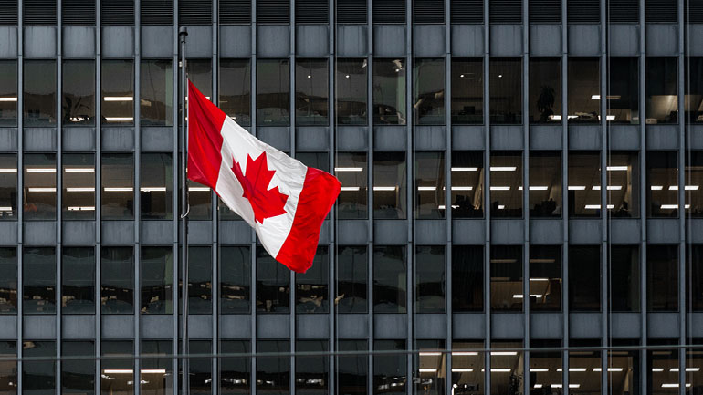 A waving Canadian flag in front of a large city skyscraper. 