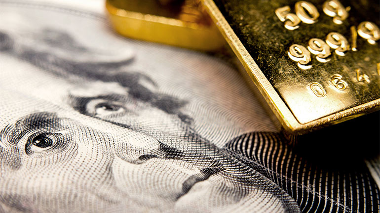 Closeup of a gold bar and an American 20-dollar bill.