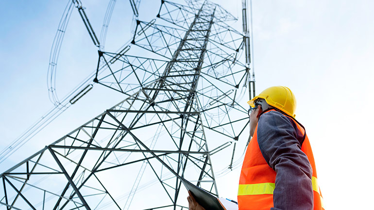 Utilities worker looking up at a high voltage tower