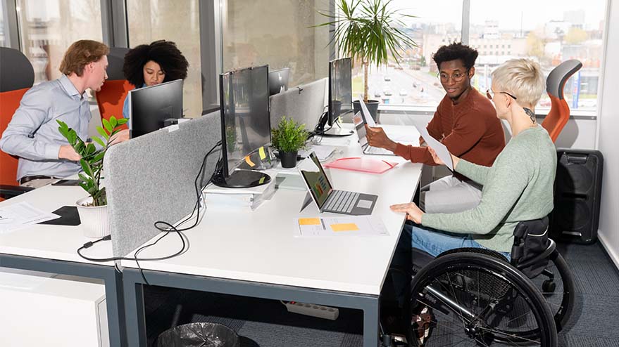 Employee using a wheelchair collaborates with coworkers in an office workspace.