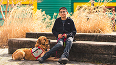 Un garçon assis sur des marches en pierre avec un chien d’assistance à ses pieds 