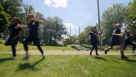 Children in school uniforms run and play on a grassy field outdoors.