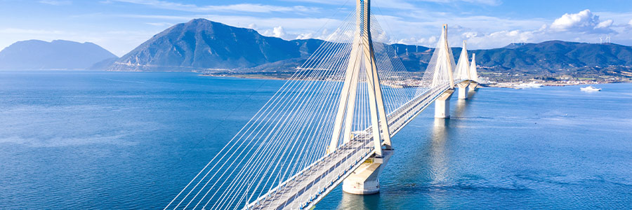 A large bridge over a body of water with a city, mountains and wind turbines in the distance.