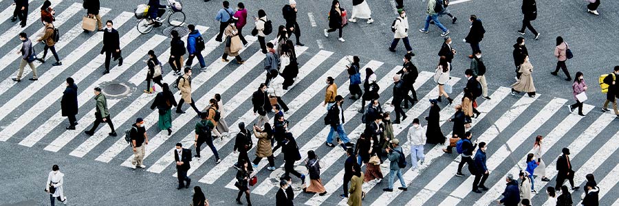 A large group of people crossing a wide, striped crosswalk in an urban setting.