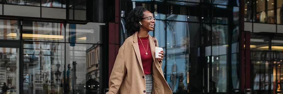 Person walking outside a modern office building holding shopping bags and a takeaway coffee cup.