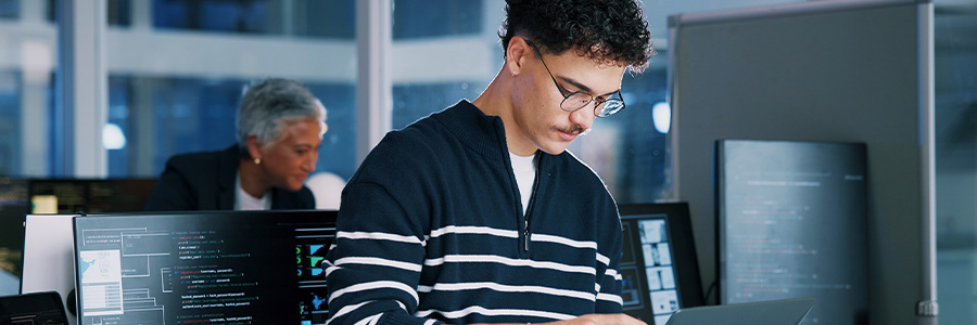 Person working on a laptop in a modern office with multiple monitors displaying code.
