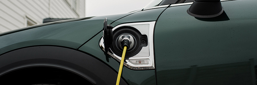 Electric car charging cable plugged into an electric vehicle’s side port outside a suburban house.