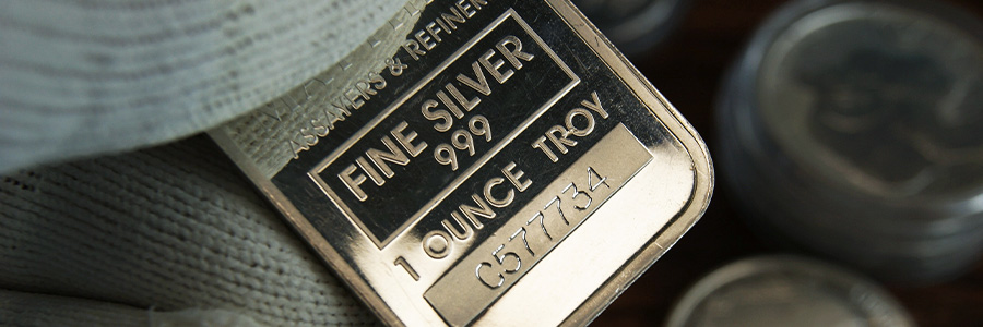 Fine silver bar held in gloved hand, with coins in the background.