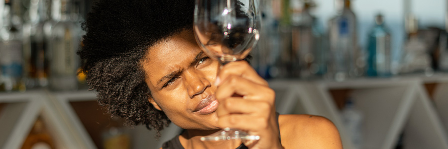 Person inspecting an empty wine glass in a bar setting, with bottles blurred in the background.
