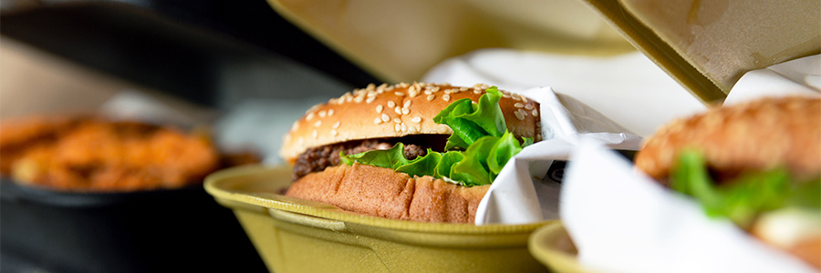 Closeup of a hamburger and other fast food in take-out containers.
