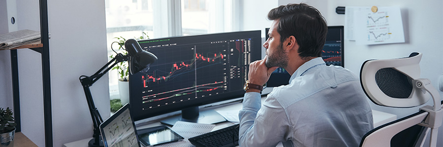 A businessperson studying data charts on computer monitors.