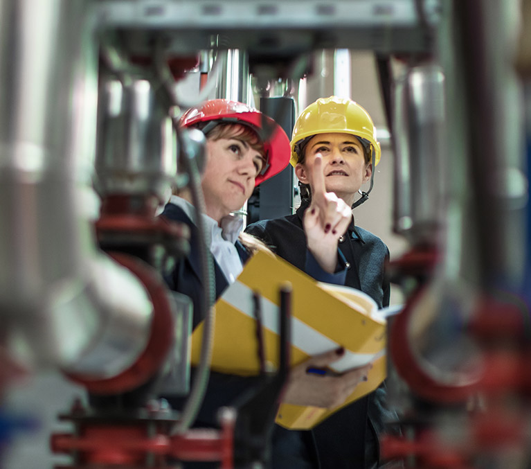 Deux professionnelles portant un casque de construction examinent de la machinerie.