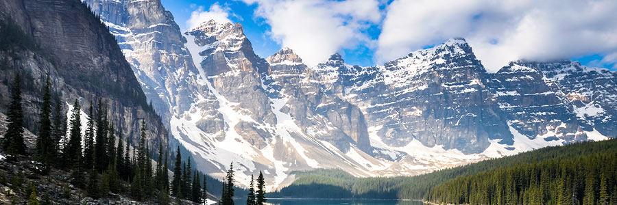 Wide landscape view of the Canadian Rocky Mountains with a blue lake in the foreground.
