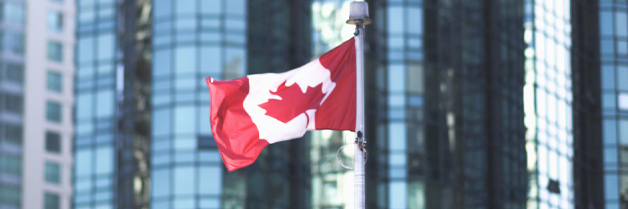 Canadian flag flying in front of downtown office towers.