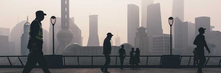Pedestrians walking along Shanghai waterfront with city skyline in haze.