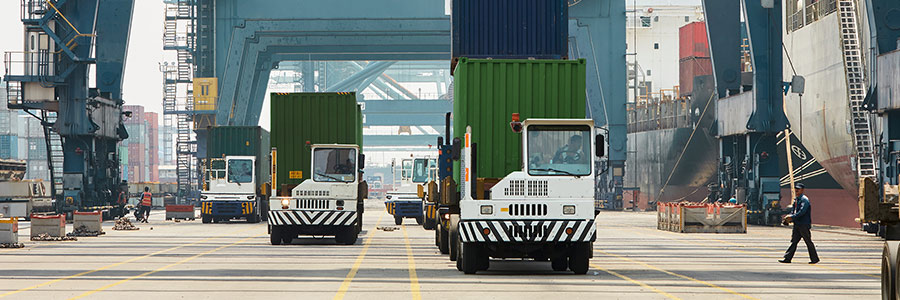 Shipping containers being transported by terminal trucks at a busy cargo port.