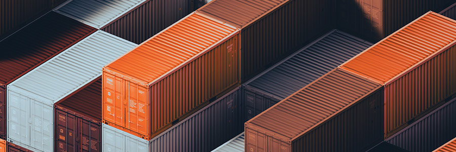 Stacked shipping containers in a cargo yard, representing global trade and commodities logistics.