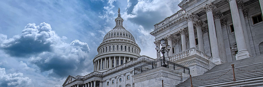 The United States Capitol building with its iconic dome, marble columns and grand staircase under a dramatic cloudy sky.