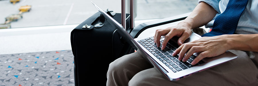 Person working on a laptop at an airport with luggage nearby.