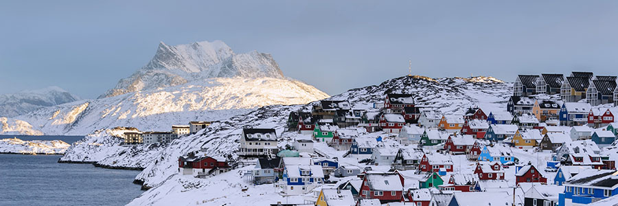Snow-covered coastal town in Greenland with colorful houses and mountains in the background.