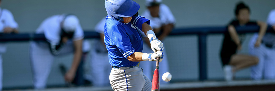 Baseball player in blue uniform swinging a bat as a pitch approaches, with opposing team players in the background.