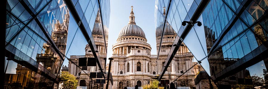 St. Paul’s Cathedral in London, a historic landmark known for its iconic dome and role in British cultural and religious history, viewed between modern glass buildings with people walking in the foreground.
