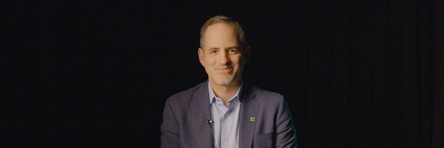 Person seated on stool in dark studio, wearing suit, with “Recording—Studio in Use” sign in foreground.