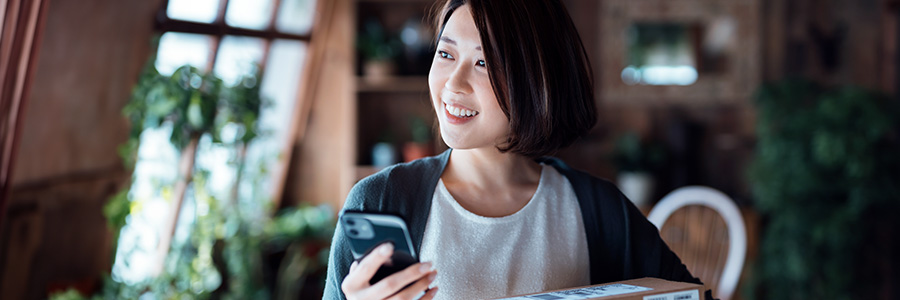 A woman holding a smartphone and a stack of postal packages.