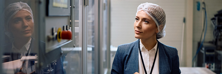 Person in a hairnet and business attire using a tablet in a food production facility.