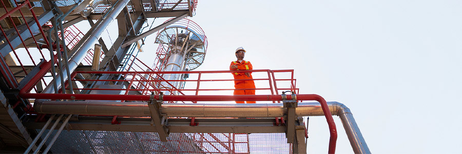 Industrial worker in safety gear standing on a platform at an industrial facility.