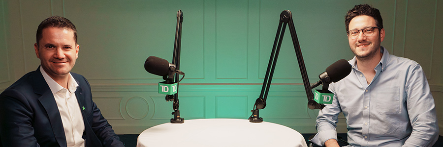 Two podcast speakers seated at a table with microphones in a studio recording setup.