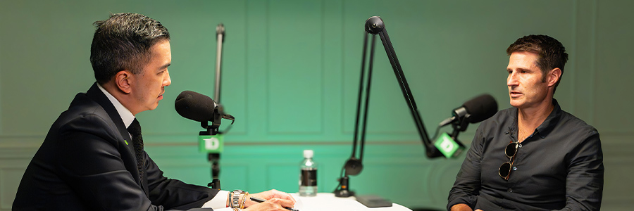 Podcast-style interview between two speakers seated at a table with microphones.