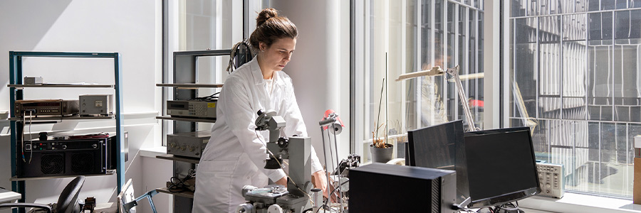 Scientist using a microscope and laboratory equipment in a bright research lab.