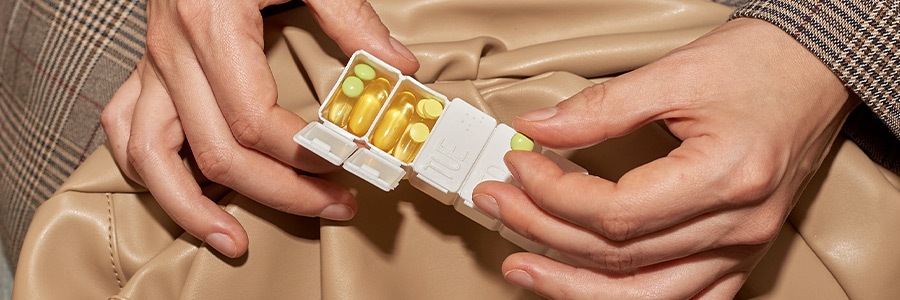 Hands holding a pill organizer containing yellow capsules and tablets.