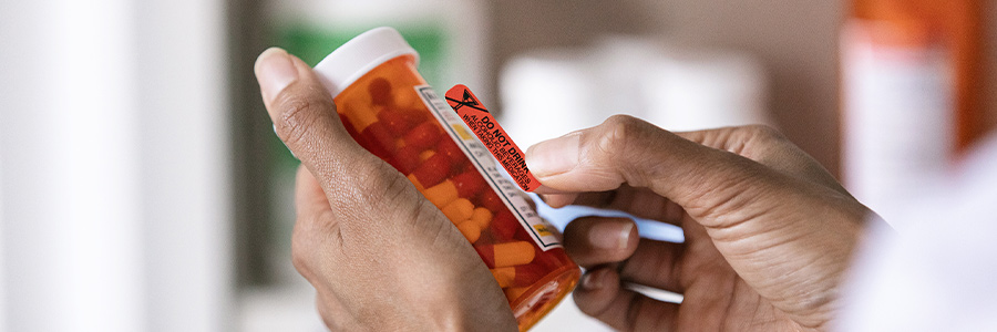 Close-up of a hand holding a prescription medication bottle with a warning label.