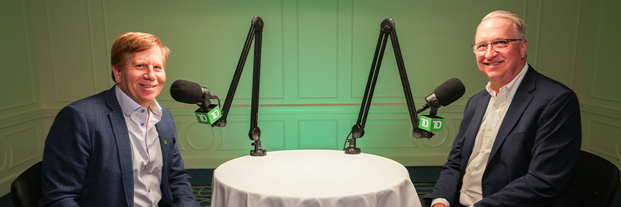 Two podcast guests seated at a table with microphones in a recording studio.
