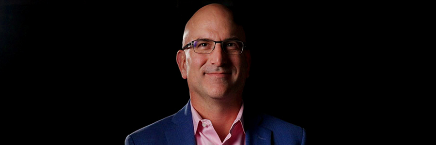 Person wearing glasses and a blue blazer against a black background.