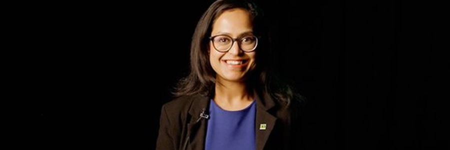 Person wearing glasses and a dark blazer against a black background.