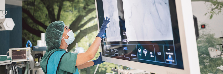 Healthcare professional reviewing medical imaging on a large monitor in a clinical procedure room.