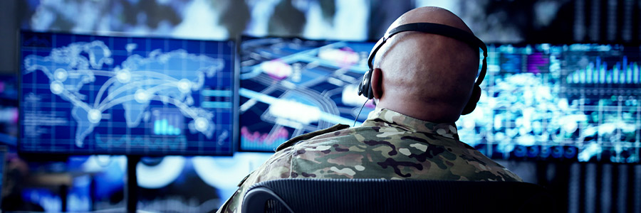 Military analyst monitoring digital maps and data on multiple screens.
