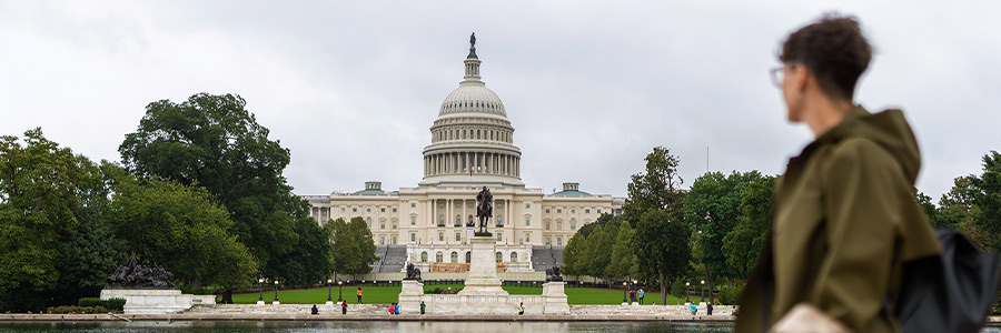 View of the United States Capitol across a reflecting pool, with a person walking in the foreground.