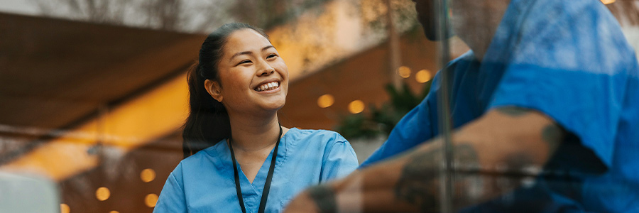 Healthcare worker in blue scrubs talking with a colleague indoors.