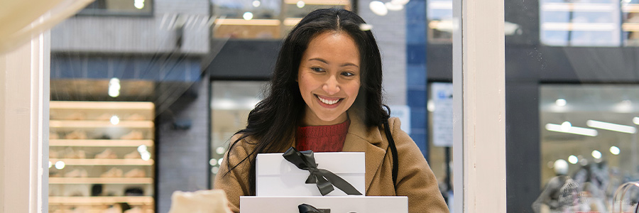 Person holding stacked gift boxes behind a storefront window.