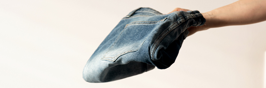 Light-wash denim jeans held above a folded stack of jeans.