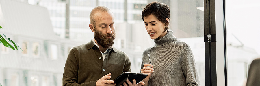 Two people reviewing documents on a tablet in a modern office.