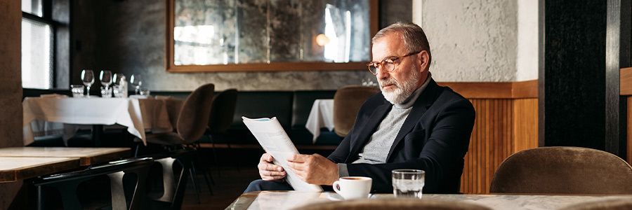 Person reading a document at a café table with a coffee and glass of water nearby.