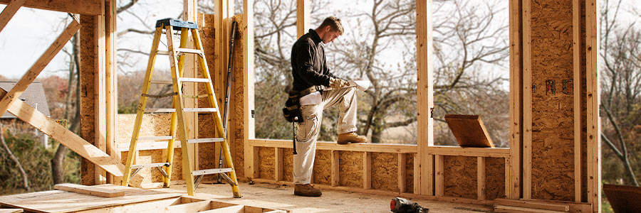Construction worker reviewing plans inside a wood-framed house under construction.