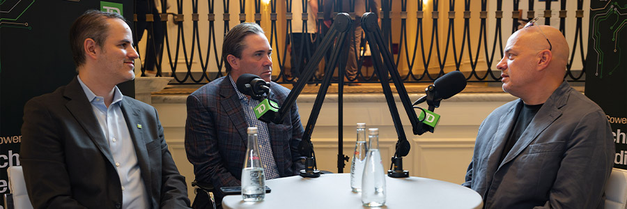 Podcast-style interview with three people seated around microphones at a table at a conference.